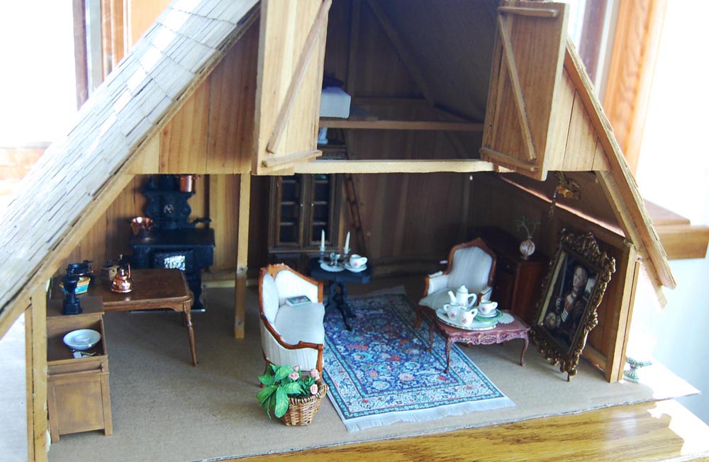 Photograph of a miniature cottage set up in an old wooden manger with miscellaneous Victorian era furniture and decorations.