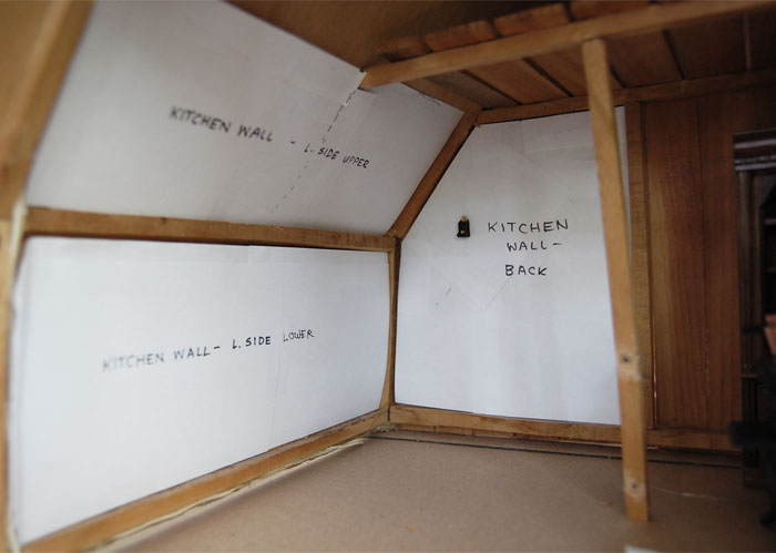 Photo of interior wall of a miniature house with templates on the walls for the back, upper, and lower left sides of kitchen